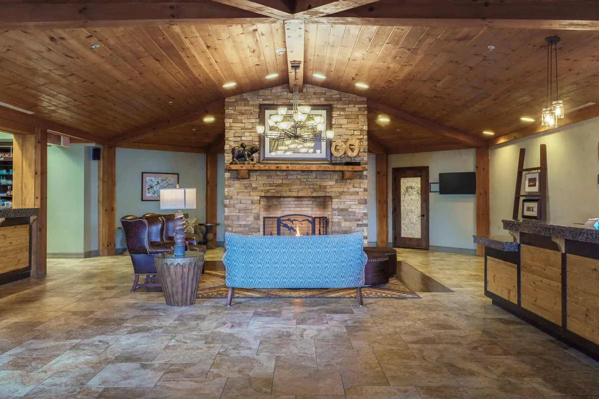 A warm, inviting space with a blue sofa arranged in front of a fireplace, wooden ceiling beams overhead, and a stylish stone wall accent. The scene exudes coziness, perfect for evenings of relaxation or lively conversation.