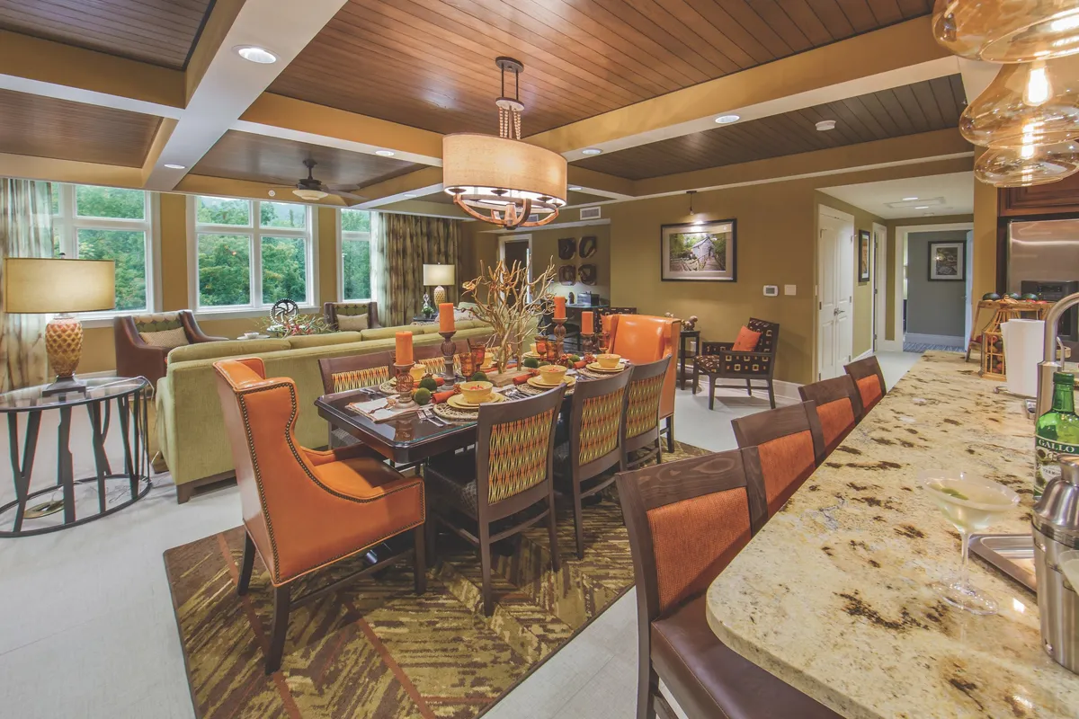 Open-concept interior showcasing a well-set dining table, a comfortable sofa arrangement, and a kitchen bar area. The layout encourages group interaction, from shared meals to casual conversations, all in a welcoming, sunlit space.