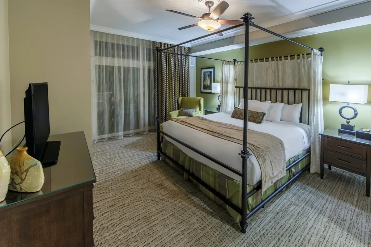 A serene bedroom featuring a canopy bed, plush armchair, matching nightstands, and decorative artwork. The space is bathed in gentle natural light, creating a welcoming atmosphere ideal for relaxation after a day of family activities.