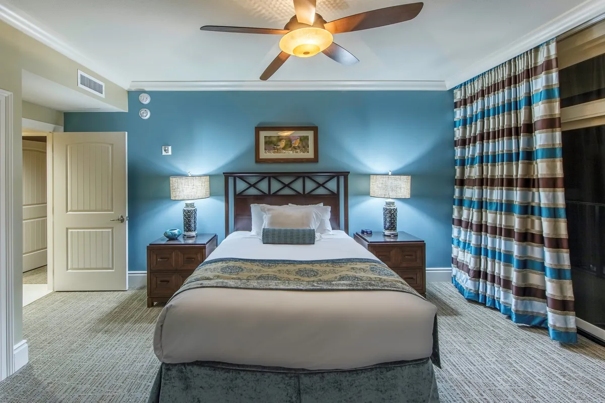 A calm and inviting bedroom with a comfortable bed, nightstands, soft curtains, and a ceiling fan. The room is designed for restful sleep or quiet moments with a book, emphasizing the villa’s private, relaxing atmosphere.