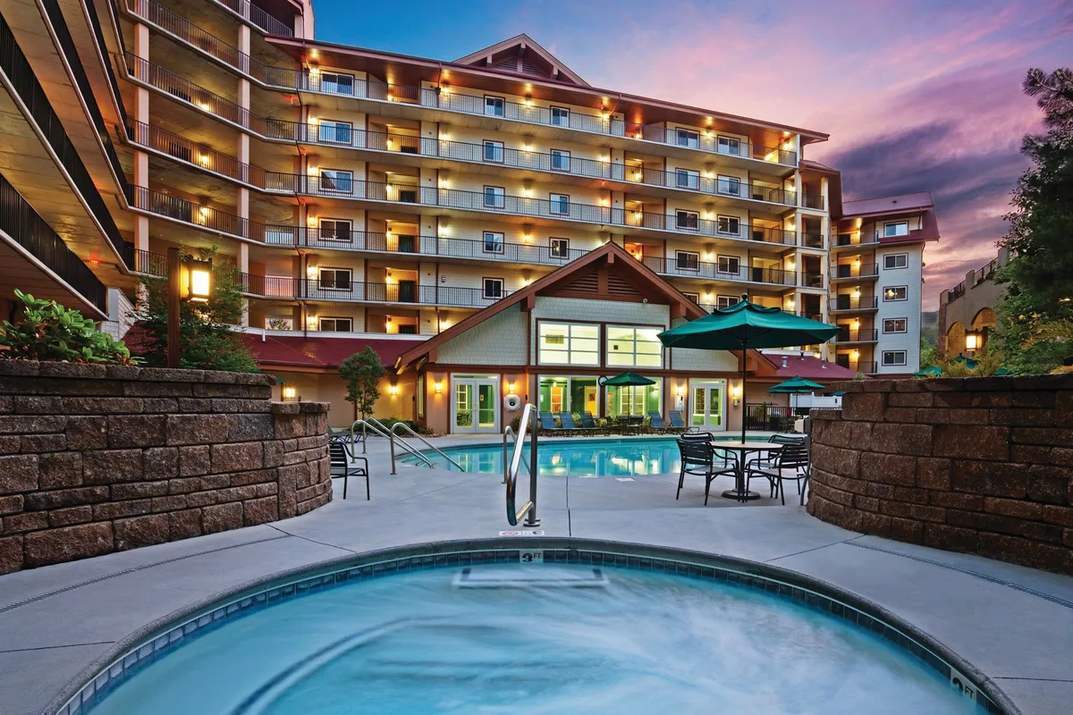 An inviting exterior view featuring a spacious swimming pool, bubbling hot tub, multiple lounge chairs, and the resort’s facade in the background. The scene suggests opportunities for sunset swims, soaking in the hot tub, and socializing outdoors.