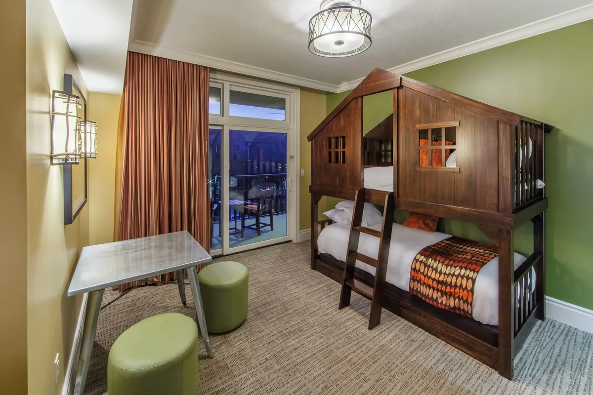 A fun and inviting bedroom featuring a sturdy bunk bed, a small table, and cozy curtains. The playful setup is ideal for families or groups with children, providing a versatile sleeping option in a warm and welcoming atmosphere.